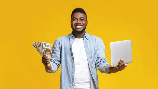 在黄色背景下拿着钱和笔记本电脑的快乐的非洲男人 — 图库照片