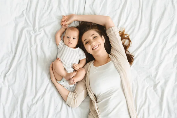 Sonriente madre con su lindo bebé acostado juntos en la cama — Foto de Stock