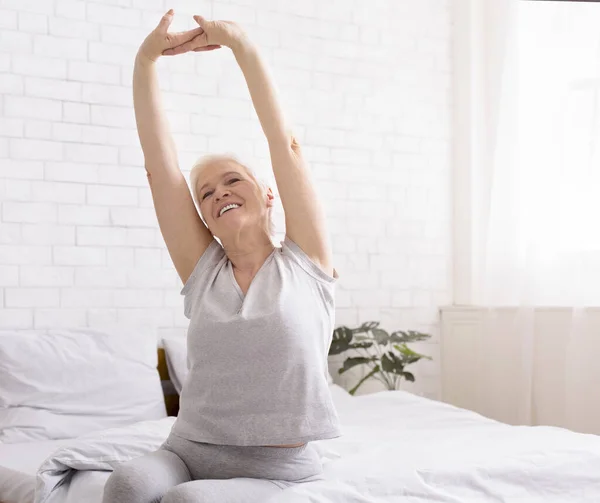 Well-slept senior lady stretching with arms raised in bed — Stock Photo, Image