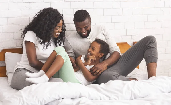 Чёрные родители щекочут свою дочь, лежа вместе в постели. — стоковое фото