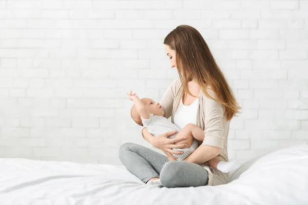 Jovem mãe sentada na cama com bebê recém-nascido nos braços — Fotografia de Stock