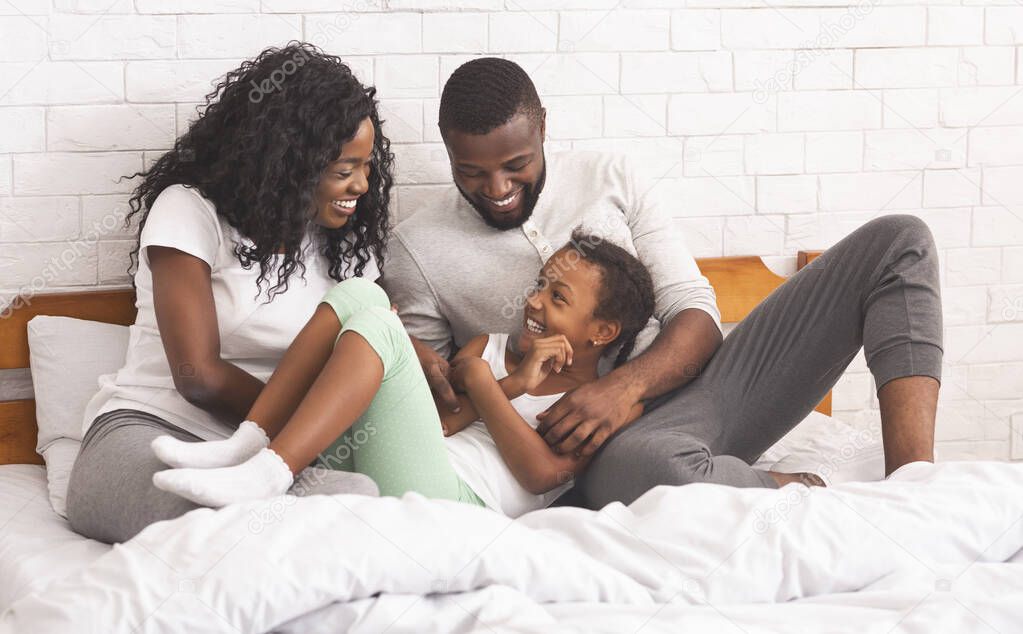 Black parents tickling their daughter while lying in bed together