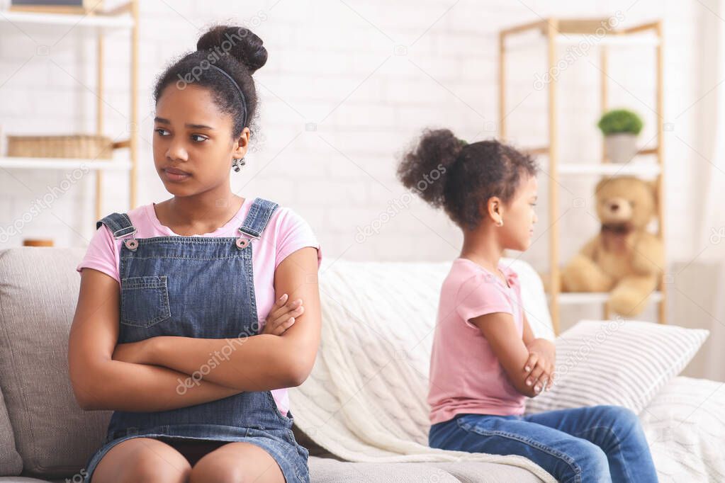 African american sisters sitting back to back on couch