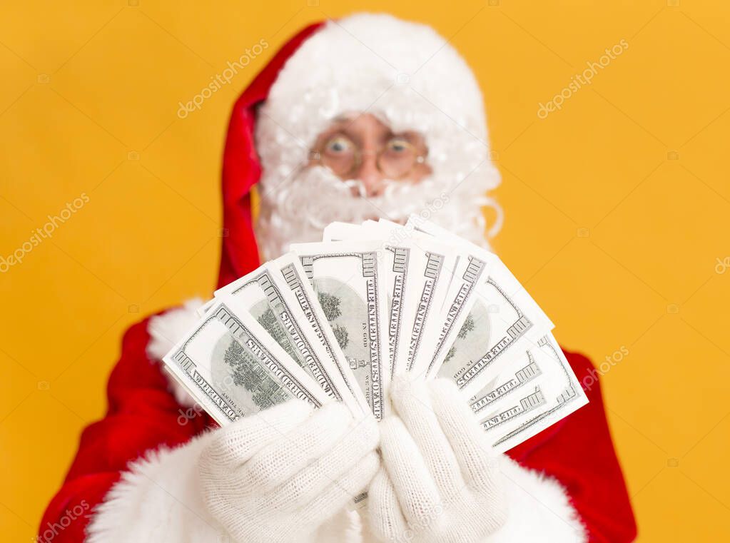 Rich Santa Claus showing many dollar banknotes on orange