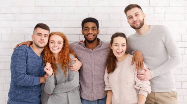 Bir grup mutlu arkadaş kameraya sarılıyor ve gülümsüyor.