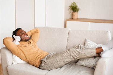 Kulaklıklı Afro-Amerikalı adam evdeki koltukta uzanıyor.