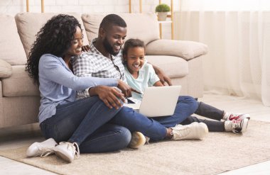 Üç kişilik siyah bir aile evde dizüstü bilgisayar kullanıyor.