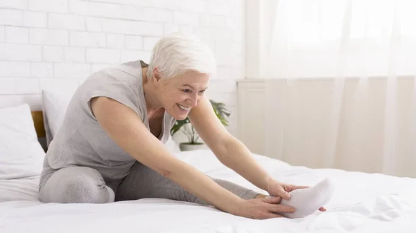 Señora mayor activa estirando sus piernas y haciendo yoga en su cama — Foto de Stock