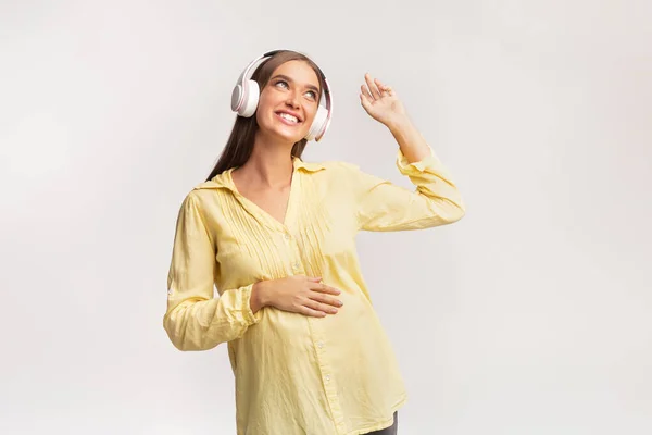 Zwangere vrouw in hoofdtelefoon luisteren naar muziek over witte achtergrond — Stockfoto