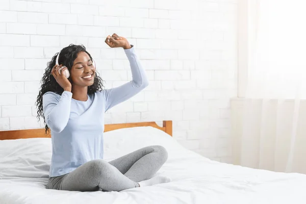 Linda chica negra escuchando música y bailando en la cama —  Fotos de Stock