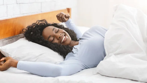 Szczęśliwa afrykańska młoda kobieta rozciągająca się w łóżku — Zdjęcie stockowe