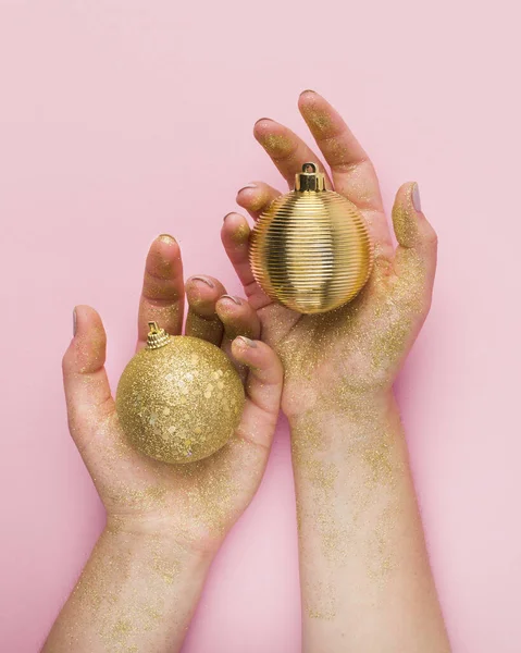 Закрыть руки женщины с золотыми шариками на розовом фоне — стоковое фото