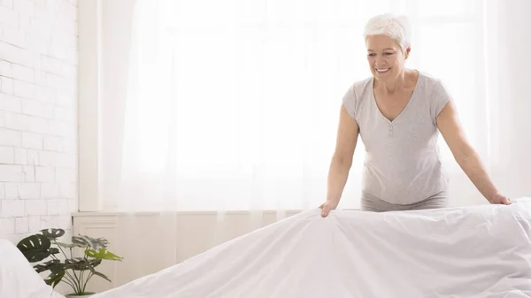 Ηλικιωμένη γυναίκα στρώνει κρεβάτι και οργανώνει δωμάτιο το πρωί — Φωτογραφία Αρχείου