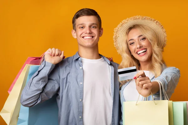 Joyful young couple recommending credit card and holding shopping bags