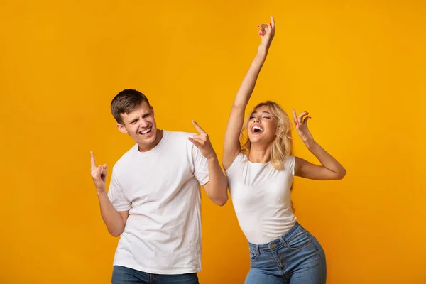Carefree young couple dancing on yellow studio background — Stock Photo, Image