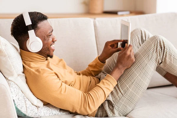 Mann mit Kopfhörer und Tablet entspannt auf Sofa zu Hause — Stockfoto