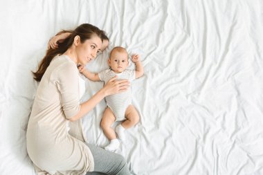 Anne yeni doğmuş tatlı bir bebekle uzanıyor ve ona şefkatle sarılıyor.