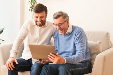 Orta yaşlı bir adam ve yaşlı bir baba dizüstü bilgisayar kullanıyor.