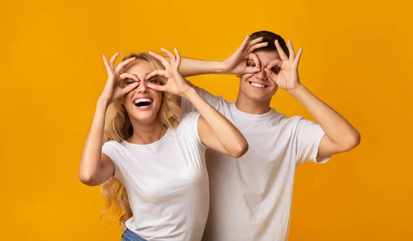 Alegre millennial pareja engañando juntos haciendo divertido gafas con los dedos —  Fotos de Stock