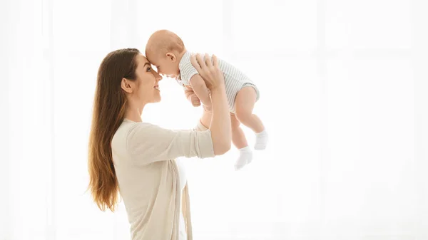 Madre sollevare il suo bambino contro la finestra a casa — Foto Stock