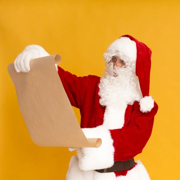 Santa Claus leyendo la lista de deseos de Navidad sobre fondo naranja — Foto de Stock