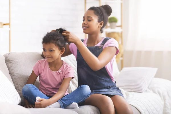Cuidar a una adolescente africana cepillándose el pelo de su hermana pequeña en casa —  Fotos de Stock