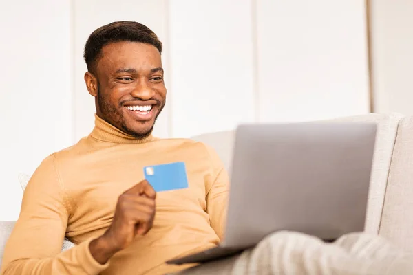 Hombre que sostiene la tarjeta de crédito usando el ordenador portátil de compras en línea en casa — Foto de Stock
