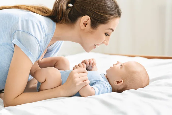 Young mother playing with her cute newborn baby in bed — Stock Photo, Image