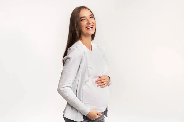 Feliz mujer embarazada tocando el vientre y riendo en el estudio —  Fotos de Stock