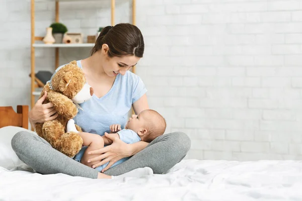 Joven madre sosteniendo oso de peluche, jugando con su bebé recién nacido — Foto de Stock