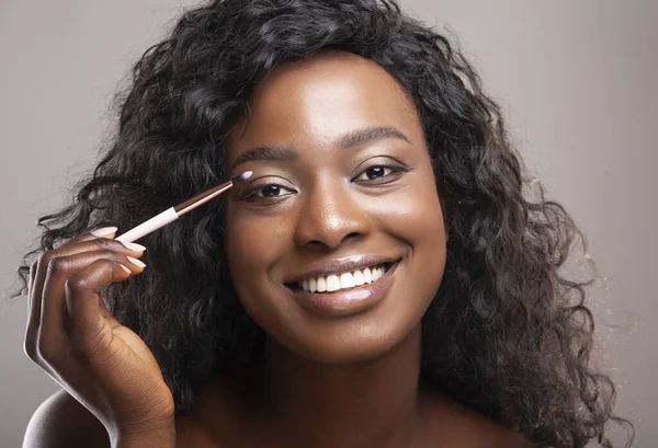 Retrato de cerca de una atractiva mujer negra aplicando sombras de ojos con pincel — Foto de Stock