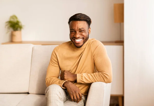 Afro cara sorrindo para câmera sentado no sofá em casa — Fotografia de Stock