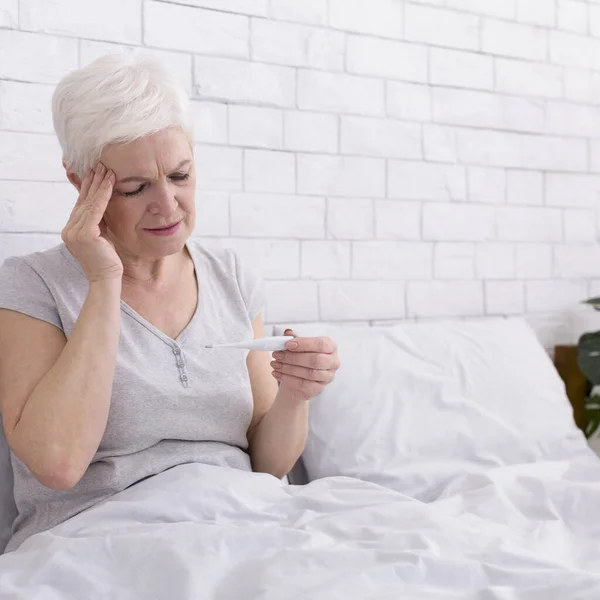 Nemocná starší dáma s horečkou měření tělesné teploty v posteli — Stock fotografie