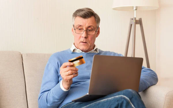 Старший чоловік використовує кредитну картку і ноутбук сидить на дивані — стокове фото
