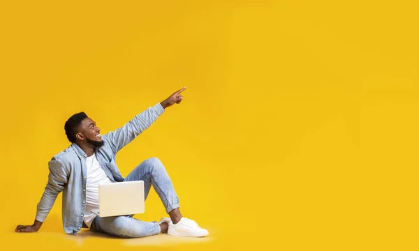 Afrikai férfi ül laptoppal és mutat a másolás tér — Stock Fotó