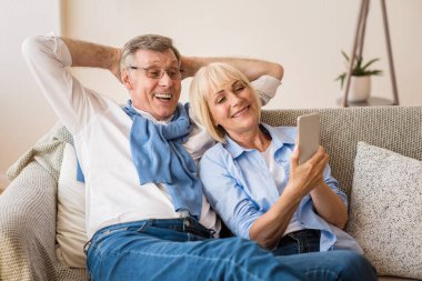 Mutlu olgun çift cep telefonu kullanıyor, internette sörf yapıyor.