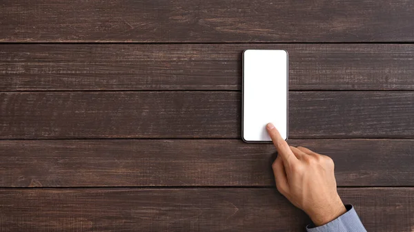 Male hand touching blank smartphone screen over dark wooden background