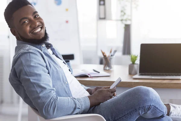 Porträtt av glada afrikanska amerikanska anställd med hjälp av smartphone på arbetsplatsen — Stockfoto