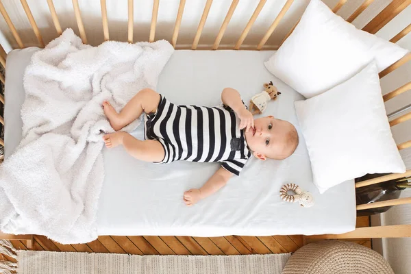 Цікава дитина лежить у дитячому ліжечку і жує палець — стокове фото