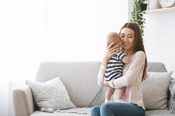 Madre sosteniendo tiernamente a su bebé recién nacido mientras está sentada en el sofá — Foto de Stock