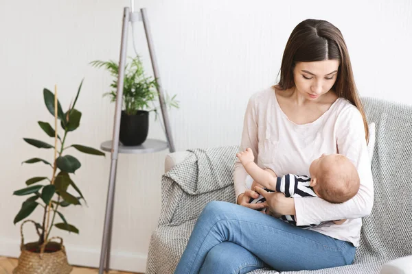 Joven mamá sentada en el sofá con el bebé recién nacido en las manos —  Fotos de Stock