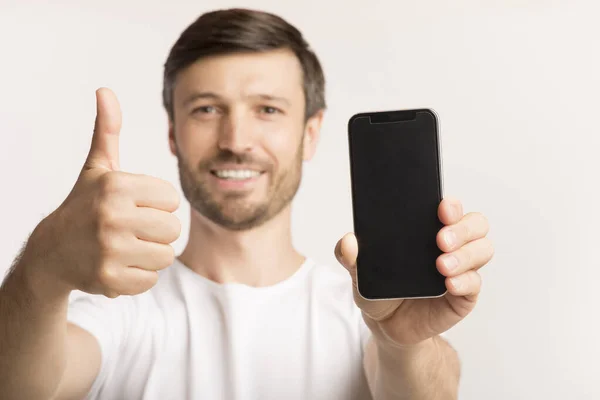 Mann hält Handy mit leerem Bildschirm und gestikuliert Daumen hoch im Studio — Stockfoto