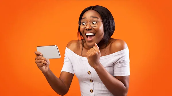 Счастливая афроамериканка с сотовым телефоном на апельсиновом фоне — стоковое фото