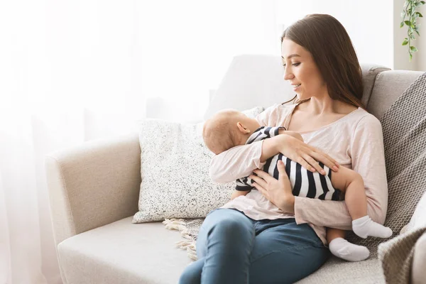 아름다운 엄마 가 집에서 소파에 앉아 갓난 아기를 안고 있는 모습 — 스톡 사진
