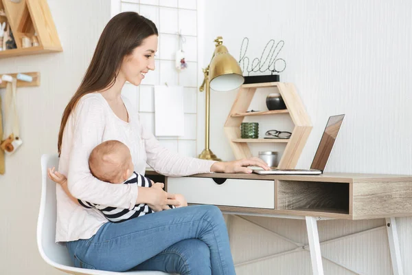 Ung mamma arbetar på laptop med barn i famnen — Stockfoto