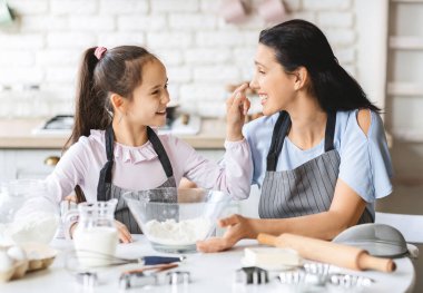 Sevimli bir kız mutfakta annesiyle oynuyor ve gülüyor.