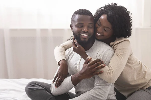 Kärleksfull fru kramande make från ryggen, sitter på sängen — Stockfoto