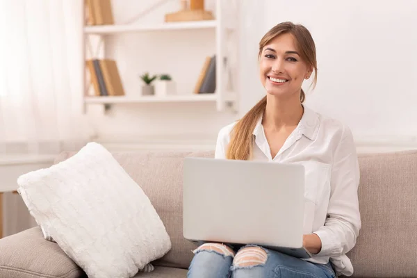 在笔记本电脑上工作的快乐女人在家里坐在沙发上 — 图库照片