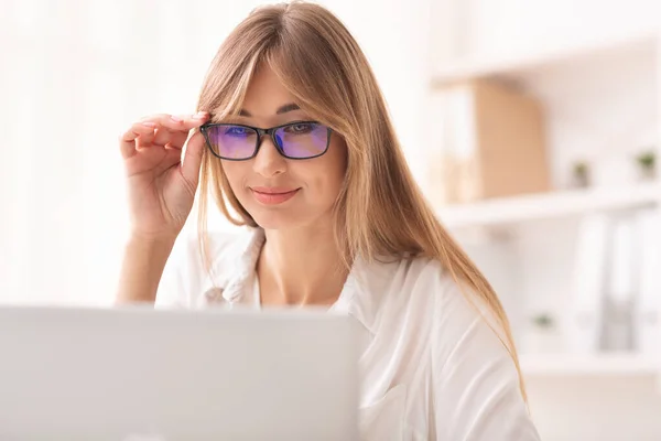 Mosolygó hölgy néz át a szemüveg a laptop dolgozik az irodában — Stock Fotó