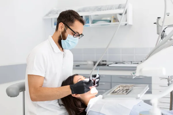 Kadın hastaya dişlerini dolduran gözlüklü dişçi doktor. — Stok fotoğraf